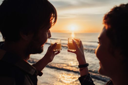 Man and woman drink orange juice against background of sunrise, young couple meets dawn on the seashore