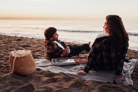 Young couple having picnic on beach at dawn, woman and man meeting sunrise together on the sea