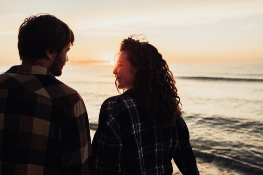 Woman and man holding hands together and walking along sea coast at dawn, young couple meeting sunrise together