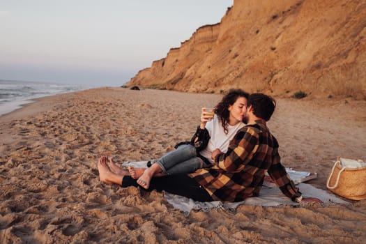 Young couple kissing on the beach at dawn, woman and man meeting sunrise together on the sea with scenic coastline on background