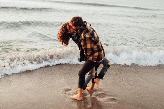 Young woman and man hugging and kissing together while standing on seashore at dawn