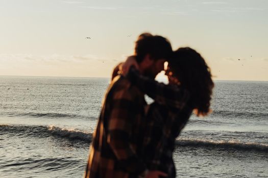 Silhouette of blurred woman and man hugging with sea on the background, young couple fall in love, focus on the waves