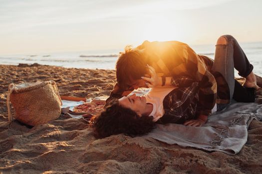 Young couple in love spending time on seashore, man kissing woman that laying on the ground against the background of the sea and sunlight