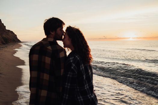 Focus on the sunrise and sea, young couple, woman and man holding by hands together and walking along sea coast at dawn