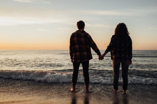 Young couple meeting sunrise on seashore, man and woman holding by hands standing in water