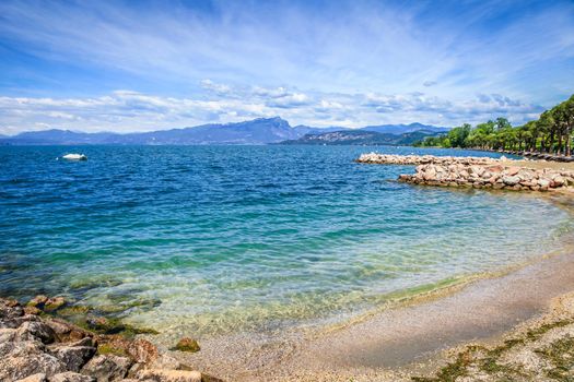 Idyllic lake Garda coastline in Lazise with boat and mountains, Northern Italy