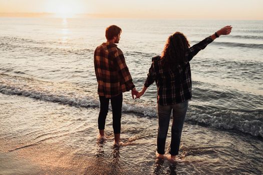 Young couple meeting sunrise on seashore, man and woman holding by hands standing in water