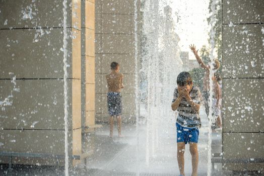 Boy having fun in water fountains. Child playing with a city fountain on hot summer day. Happy kids having fun in fountain. Summer weather. Active leisure, lifestyle and vacation.