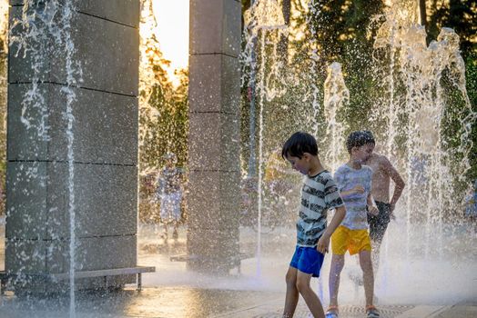 Boys jumping in water fountains. Children playing with a city fountain on hot summer day. Happy friends having fun in fountain. Summer weather. Friendship, lifestyle and vacation.