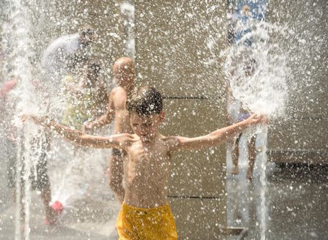 Boy having fun in water fountains. Child playing with a city fountain on hot summer day. Happy kids having fun in fountain. Summer weather. Active leisure, lifestyle and vacation.