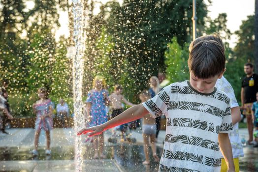 Boys jumping in water fountains. Children playing with a city fountain on hot summer day. Happy friends having fun in fountain. Summer weather. Friendship, lifestyle and vacation.