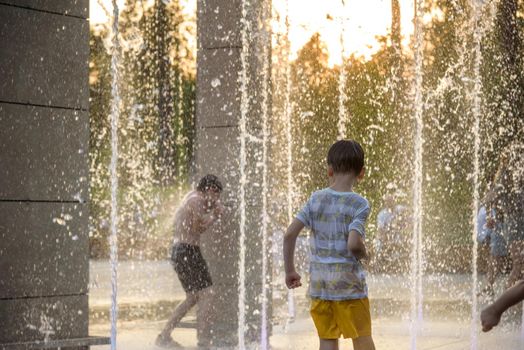 Boy having fun in water fountains. Child playing with a city fountain on hot summer day. Happy kids having fun in fountain. Summer weather. Active leisure, lifestyle and vacation.