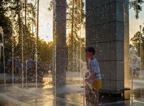 Boy having fun in water fountains. Child playing with a city fountain on hot summer day. Happy kids having fun in fountain. Summer weather. Active leisure, lifestyle and vacation.