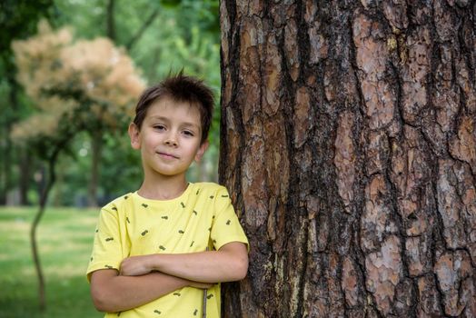 Little boy hugs a tree trunk - children love the nature, sustainability concept. Happy smiling kid look directly to camera. Save the nature.