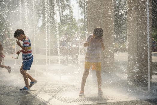 Boy having fun in water fountains. Child playing with a city fountain on hot summer day. Happy kids having fun in fountain. Summer weather. Active leisure, lifestyle and vacation.