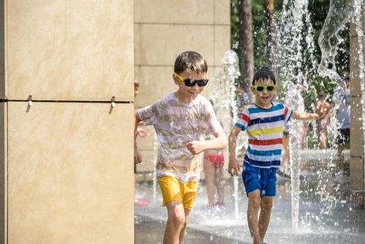 Boy having fun in water fountains. Child playing with a city fountain on hot summer day. Happy kids having fun in fountain. Summer weather. Active leisure, lifestyle and vacation.