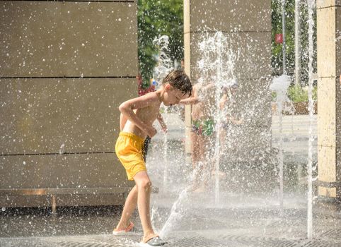 Boy having fun in water fountains. Child playing with a city fountain on hot summer day. Happy kids having fun in fountain. Summer weather. Active leisure, lifestyle and vacation.