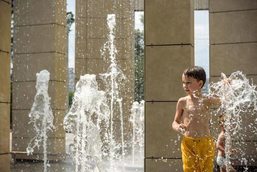 Boy having fun in water fountains. Child playing with a city fountain on hot summer day. Happy kids having fun in fountain. Summer weather. Active leisure, lifestyle and vacation.