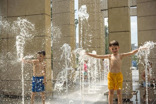 Boy having fun in water fountains. Child playing with a city fountain on hot summer day. Happy kids having fun in fountain. Summer weather. Active leisure, lifestyle and vacation.