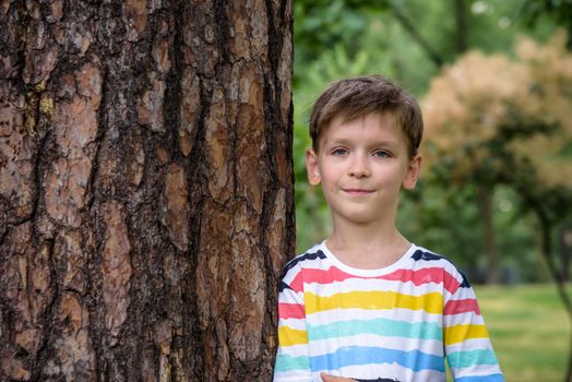 Little boy hugs a tree trunk - children love the nature, sustainability concept. Happy smiling kid look directly to camera. Save the nature.