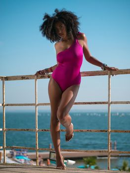 Portrait of cheerful black people, pretty happy young afro american woman smiling on sea beach. Sexy girl in pink swimsuit and jewelry enjoying nature.Lady wearing bikini.