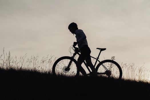 Silhouette of Professional Male Cyclist Pushing His Bike on Top of Hill at Sunset