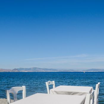 White restaurant tables on the beach in summer - travel, vacation and summer concept. The perfect lunch with a sea view