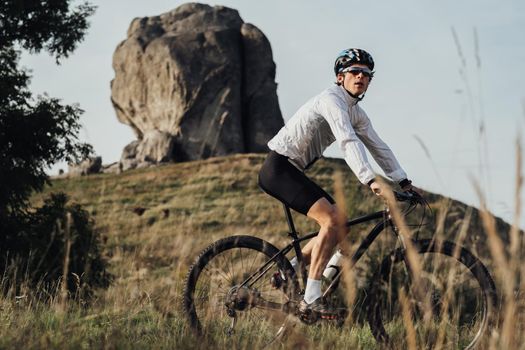 Professional Equipped Cyclist on Trail with Giant Stone, Miracle of Nature on Background, Adult Man Riding Bike Outdoors