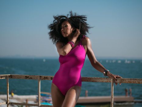 Portrait of cheerful black people, pretty happy young afro american woman smiling on sea beach. Sexy girl in pink swimsuit and jewelry enjoying nature.Lady wearing bikini.