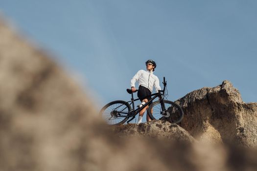 Equipped Professional Cyclist Standing with Mountain Bike on Top of Rock, Sky Background and Copy Space