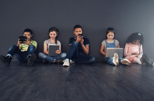 Learning to be technology literate. Studio shot of kids sitting on the floor and using wireless technology against a gray background
