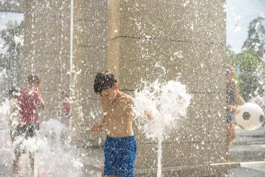 Boy having fun in water fountains. Child playing with a city fountain on hot summer day. Happy kids having fun in fountain. Summer weather. Active leisure, lifestyle and vacation.