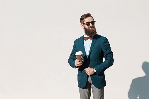 Stylish man with beard wearing a jacket, shirt and bow tie holding a coffee