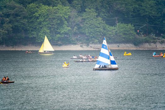 four colorful sailboats lost in the haze fog with smaller pedal row boats floating around on the cloudy naini jheel in nainital lake in uttarakhand India a popular tourist destination