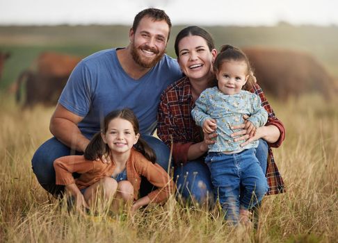 Portrait of happy family on a countryside farm field with cows in the background. Farmer parents bonding with kids on a sustainable agriculture cattle business with a smile and happiness together.