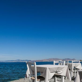 White restaurant tables on the beach in summer - travel, vacation and summer concept. The perfect lunch with a sea view