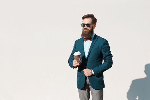 Stylish man with beard wearing a jacket, shirt and bow tie holding a coffee