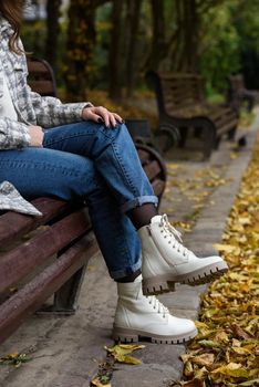 Female legs in a jeans and white fashion boots with laces. fallen leaves on the sidewalk