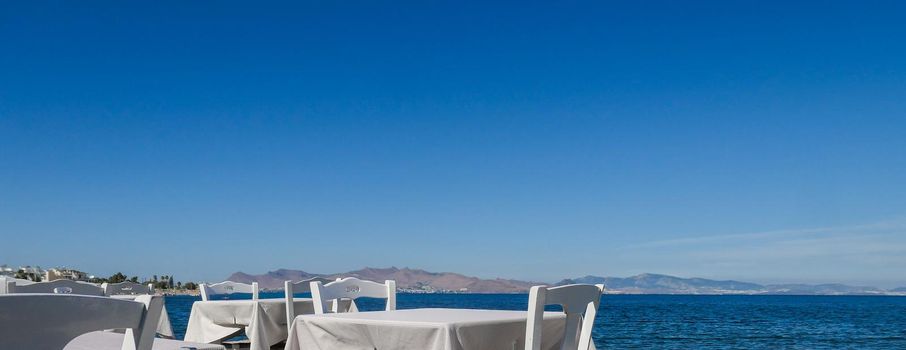 White restaurant tables on the beach in summer - travel, vacation and summer concept. The perfect lunch with a sea view