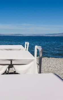 White restaurant tables on the beach in summer - travel, vacation and summer concept. The perfect lunch with a sea view