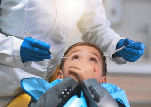 Do you promise that it wont hurt. a frightened little boy lying down on a dentist chair and holds his mouth closed to keep the dentist from working on him