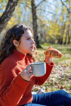 Leisure, free time. Beautiful caucasian woman in red sweater on a picnic outdoors, sitting on a plaid in autumn forest