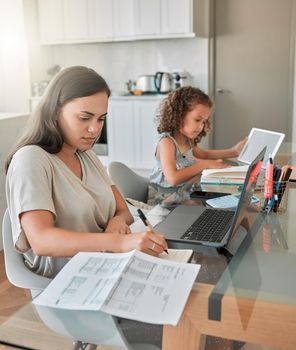 Mother and daughter being productive with remote work and homework, multitasking at a kitchen table at home. Parent and child serious while paying bills and watching an online education programme.