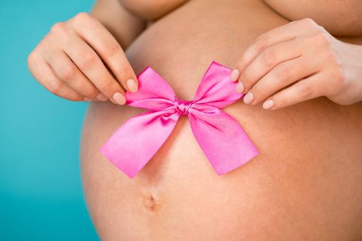 Pregnant woman holding pink bow on tummy belly background. Young girl expecting baby. Maternity, motherhood, pregnancy, love concept.