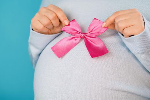 Pregnant woman holding pink bow on tummy belly background. Young girl expecting baby. Maternity, motherhood, pregnancy, love concept.
