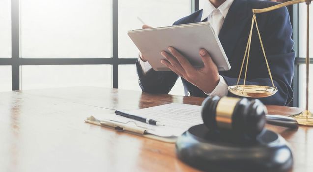 justice and law concept.Male judge in a courtroom the gavel,working with digital tablet on wood table in office.