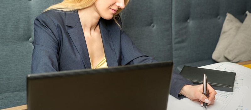 Young businesswoman sitting at the table and writing in a notebook. Adult woman working with papers at the cafe