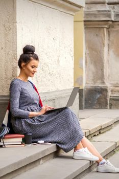 A teenage happy student working on a laptop computer on stairs outdoors