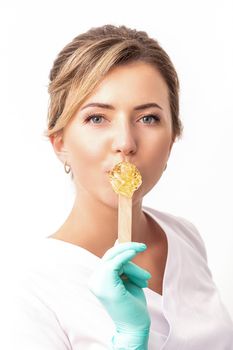 Portrait of female cosmetologist holds a wooden stick with a wax covering her lips on white background