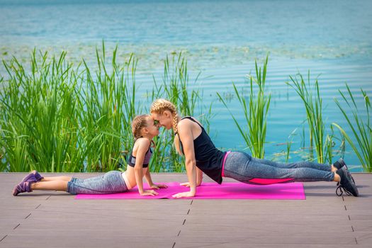 Mother and daughter doing sports exercises on the pier near the water outdoor